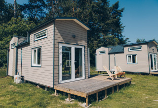A photo of the 'Koya Tiny Loft' tiny houses at Wilsumer Berge, Germany, featuring wooden decks and trees.