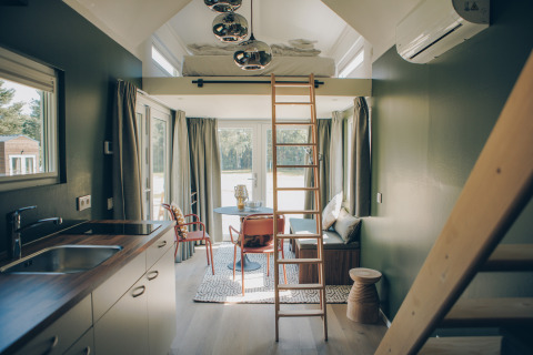 Modern, sunlit interior of Koya Tiny Loft tiny house in Germany, featuring loft bed, ladder, kitchen, and sitting area.