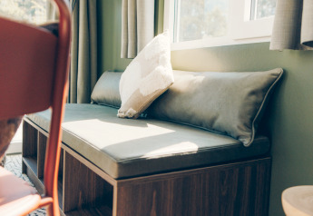 Banquette ensoleillée avec coussins près de la fenêtre dans Koya Tiny Loft, Wilsumer Berge, Allemagne.