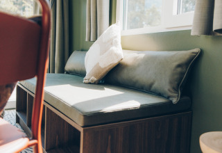 Sunny bench seating with plush cushions by the window in Koya Tiny Loft, Wilsumer Berge, Germany.