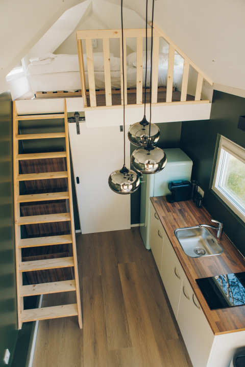 Interior of Koya Tiny Loft at Wilsumer Berge, Germany, showing a loft bed, ladder, kitchen, and lights.