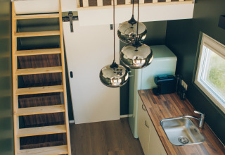 Interior of Koya Tiny Loft at Wilsumer Berge, Germany, showing a loft bed, ladder, kitchen, and lights.