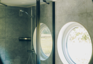 Round mirror reflecting a small bathroom with shower and circular window at Koya Tiny Loft, Wilsumer Berge.