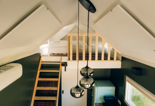 Interior of Koya Tiny Loft at Wilsumer Berge, Germany, featuring a loft bed, wooden ladder, and pendant lights.