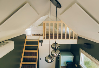 Interior of Koya Tiny Loft at Wilsumer Berge, Germany, featuring a loft bed, wooden ladder, and pendant lights.