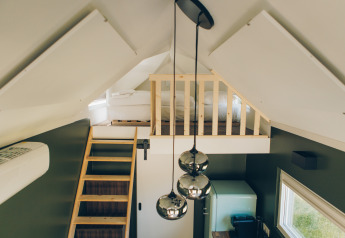 Interior of Koya Tiny Loft at Wilsumer Berge, Germany, featuring a loft bed, wooden ladder, and pendant lights.