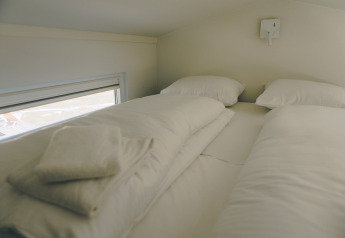 Espace nuit minimaliste avec deux lits et du linge blanc à Koya Tiny Loft, Wilsumer Berge, Allemagne.