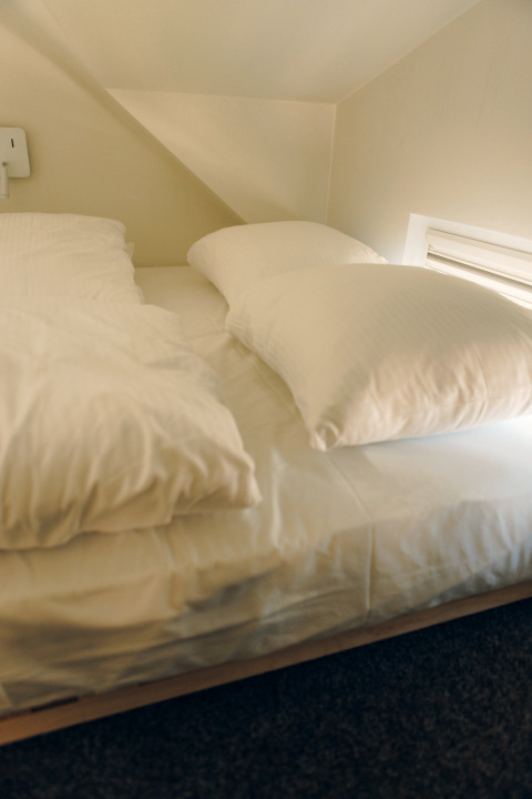 Sleeping area with sloped ceiling and single bed with white bedding, taken in Koya Tiny Loft, Wilsumer Berge, Germany.