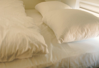 Sleeping area with sloped ceiling and single bed with white bedding, taken in Koya Tiny Loft, Wilsumer Berge, Germany.
