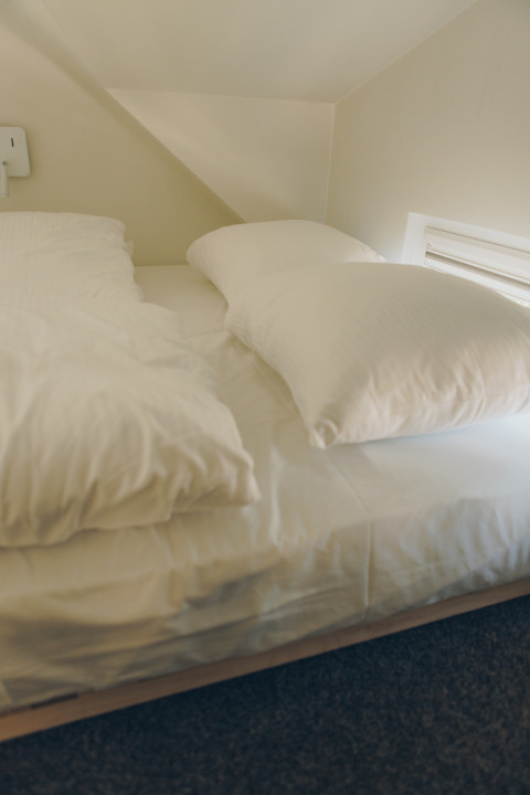Sleeping area with sloped ceiling and single bed with white bedding, taken in Koya Tiny Loft, Wilsumer Berge, Germany.