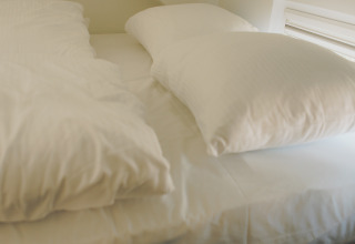 Sleeping area with sloped ceiling and single bed with white bedding, taken in Koya Tiny Loft, Wilsumer Berge, Germany.