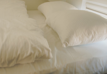 Sleeping area with sloped ceiling and single bed with white bedding, taken in Koya Tiny Loft, Wilsumer Berge, Germany.