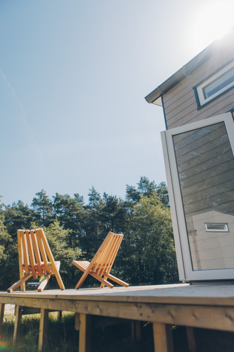 Sunny deck with two wooden chairs at Koya Tiny Loft, Wilsumer Berge, Germany, surrounded by nature.