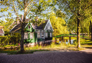 Cabañas verdes encantadoras y puente de madera en un parque vacacional de glamping junto a un canal.