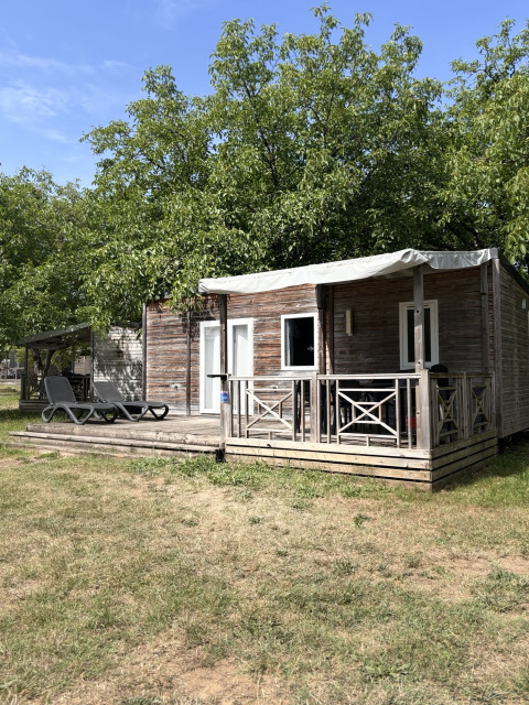Premium Mobilheim bei Flower Camping Les Ondines in Frankreich mit Holzveranda und Liegestühlen auf dem Rasen.