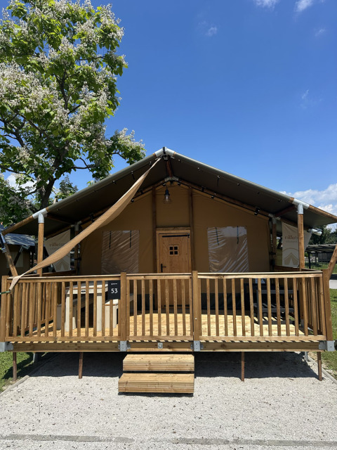Tenda safari Outback con veranda e gradini in legno, fotografata in una giornata di sole e cielo azzurro.