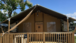 Safaritent Outback met houten veranda en trap, gefotografeerd op een zonnige dag onder blauwe lucht.