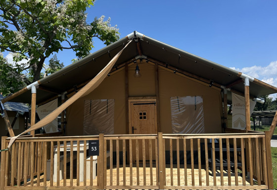 Tenda safari Outback con veranda e gradini in legno, fotografata in una giornata di sole e cielo azzurro.