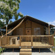 Outback safari tent with wooden deck and steps, photographed on a sunny day under a clear blue sky.