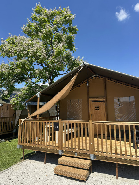 Tenda safari 'Outback' al Camping Terme Tuhelj in Croazia, veranda in legno e albero fiorito in giornata soleggiata.