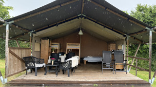 Safaritent op Camping de Regenboog in Tsjechië met overdekte veranda, stoelen en zichtbare bedden.