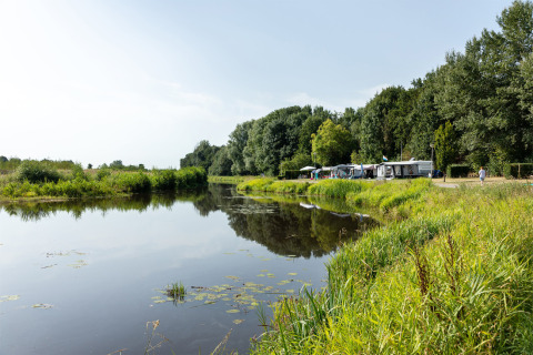 Camping junto a un lago tranquilo en Hunzepark, Drenthe, Países Bajos, rodeado de árboles y vegetación.