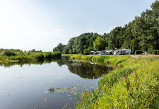 Camping junto a un lago tranquilo en Hunzepark, Drenthe, Países Bajos, rodeado de árboles y vegetación.