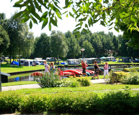 Families walking near colorful kayaks and tents at Hunzepark holiday park in Drenthe, Netherlands.