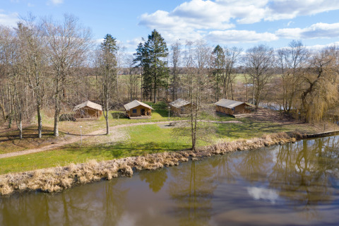 Tiendas safari junto a un estanque en Hunzepark, Países Bajos, rodeadas de árboles y naturaleza.
