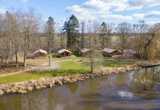 Tiendas safari junto a un estanque en Hunzepark, Países Bajos, rodeadas de árboles y naturaleza.