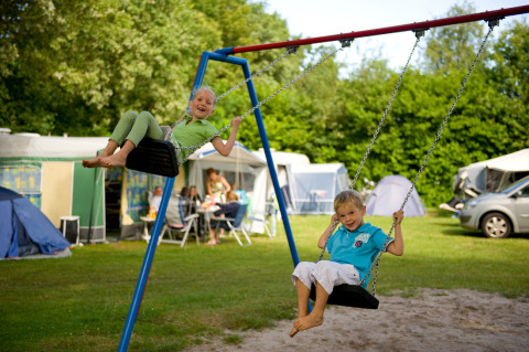 Deux enfants jouent sur des balançoires à Hunzepark, un parc de vacances à Drenthe, Pays-Bas, avec tentes derrière.