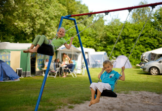 Deux enfants jouent sur des balançoires à Hunzepark, un parc de vacances à Drenthe, Pays-Bas, avec tentes derrière.