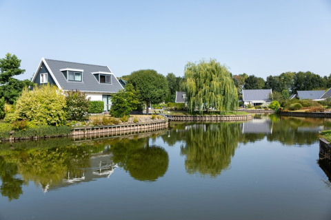 Casa junto al lago en el parque vacacional Hunzepark, Drenthe, Países Bajos, rodeada de vegetación y agua tranquila.