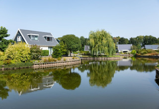 House by the lake in Hunzepark holiday park, Drenthe, Netherlands, surrounded by greenery and calm waters.