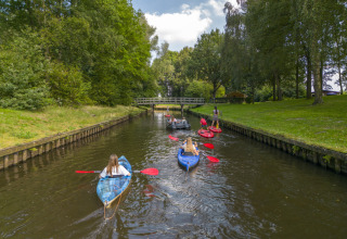 Personas remando en kayaks y canoas por un canal rodeado de árboles en Hunzepark, Drenthe, Países Bajos.