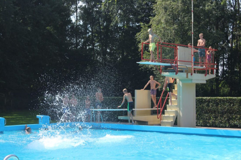 Children playing at an outdoor pool with a diving board at Hunzepark holiday park in Drenthe, Netherlands.