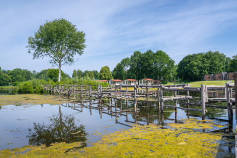 Vue sur un lac avec passerelle en bois et chalets de vacances en arrière-plan à Hunzepark, Drenthe, Pays-Bas.