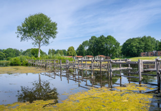 View of a lake with wooden bridge and holiday cottages in the background at Hunzepark, Drenthe, Netherlands.