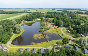 Luftfoto af Hunzepark feriepark med sø, hytter og grønne områder i Drenthe, Holland, under en blå himmel.