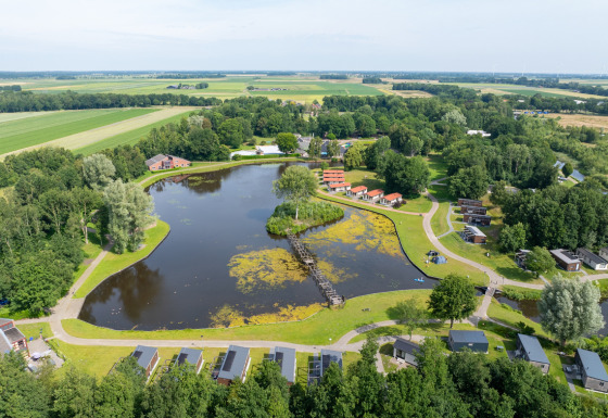 Aerial view of Hunzepark holiday park, showing a central lake, cabins, and greenery in Drenthe, Netherlands.