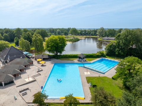 Vista aérea de Hunzepark, un parque vacacional en Drenthe, Países Bajos, con piscina, lago y vegetación.
