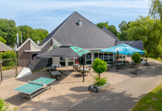 Terraza exterior con mesas, sillas y sombrillas en Hunzepark, parque vacacional en Drenthe, Países Bajos.