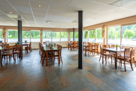 Salle à manger lumineuse et spacieuse avec grandes fenêtres et meubles en bois au Hunzepark à Drenthe.