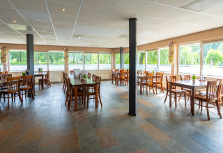 Luminoso y amplio comedor con grandes ventanales y muebles de madera en Hunzepark, Drenthe, Países Bajos.