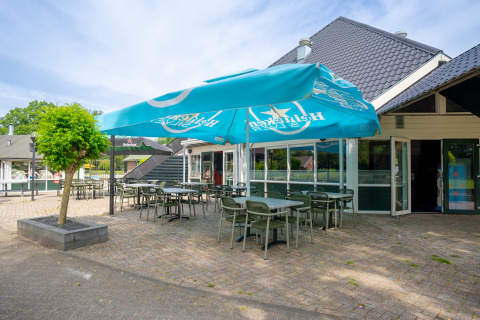 Terraza exterior con sillas verdes y sombrilla Heineken en Hunzepark, parque vacacional en Drenthe, Países Bajos.