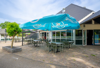 Terraza exterior con sillas verdes y sombrilla Heineken en Hunzepark, parque vacacional en Drenthe, Países Bajos.
