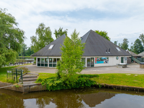 View of a building near the water at Hunzepark holiday park in Drenthe, Netherlands, surrounded by trees.
