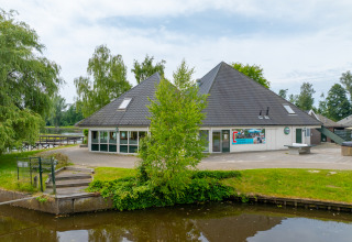 Vista de un edificio cerca del agua en Hunzepark, un parque vacacional en Drenthe, Países Bajos, con árboles.