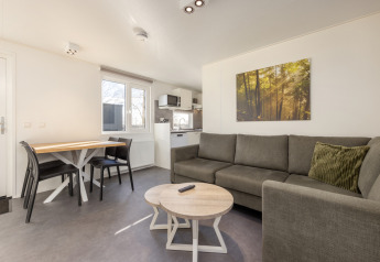 Moderne stue i Chalet Comfort 4 på Hunzepark, Nederlandene, med sofa, spisebord og lille køkken.