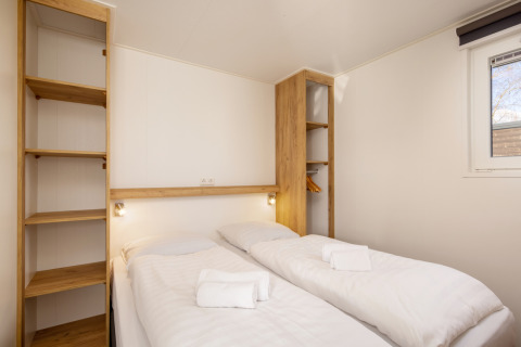 Dormitorio con dos camas individuales, ropa de cama blanca, toallas y estantes en Chalet Comfort 4, Hunzepark.